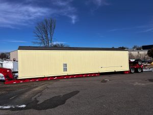A lowboy trailer carries a 45 foot long water treatment building to its destination