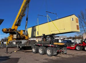 A crane lifts a packaged turnkey water treatment system on to a truck for transport and drop-in installation at a project site